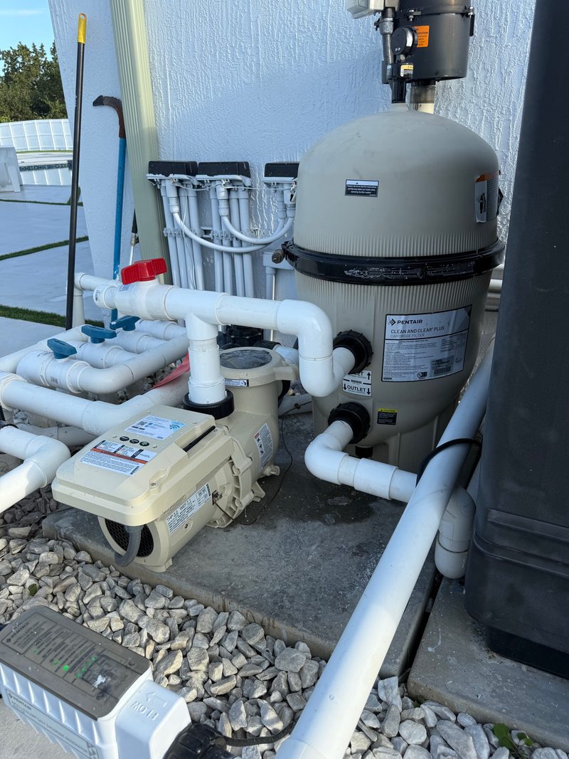 Una bomba de piscina nueva con su panel de control junto a un filtro grande, conectada con tubería blanca